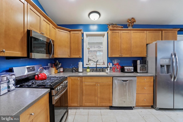 kitchen with light tile patterned floors, appliances with stainless steel finishes, brown cabinets, and a sink