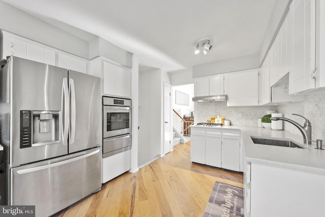 kitchen with white cabinets, tasteful backsplash, light wood-type flooring, sink, and stainless steel appliances