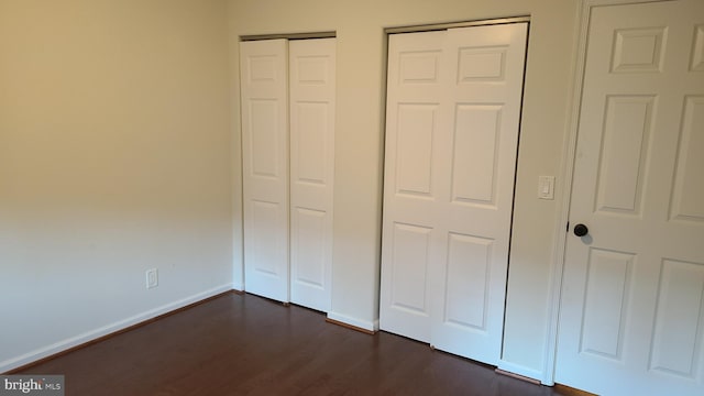 unfurnished bedroom with multiple closets and dark wood-type flooring