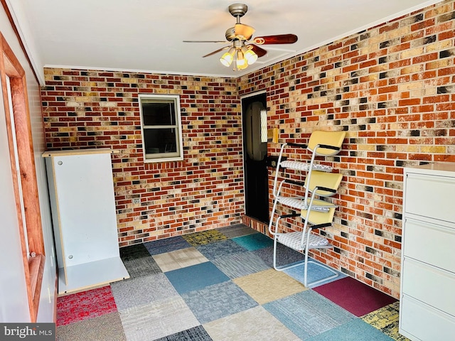 unfurnished office featuring ceiling fan, ornamental molding, and brick wall