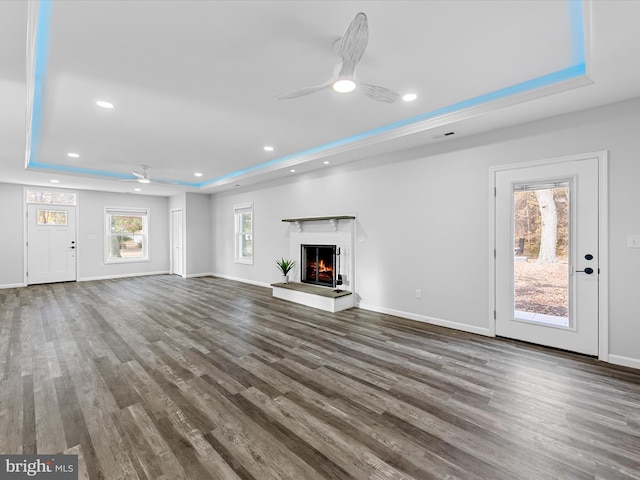 unfurnished living room featuring a fireplace, dark hardwood / wood-style flooring, a tray ceiling, and ceiling fan