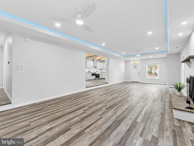 unfurnished living room featuring ceiling fan, light hardwood / wood-style floors, a raised ceiling, and a fireplace