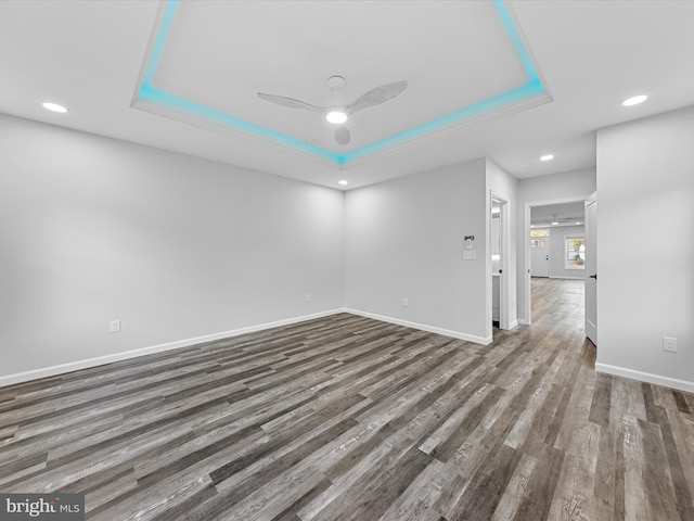 spare room with a tray ceiling, ceiling fan, and dark wood-type flooring