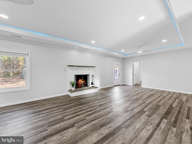 unfurnished living room featuring a brick fireplace, ceiling fan, dark hardwood / wood-style flooring, and a tray ceiling