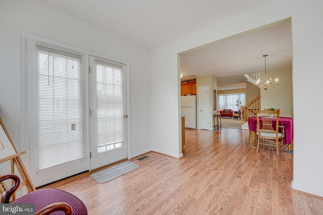 doorway with light wood-type flooring, an inviting chandelier, and plenty of natural light