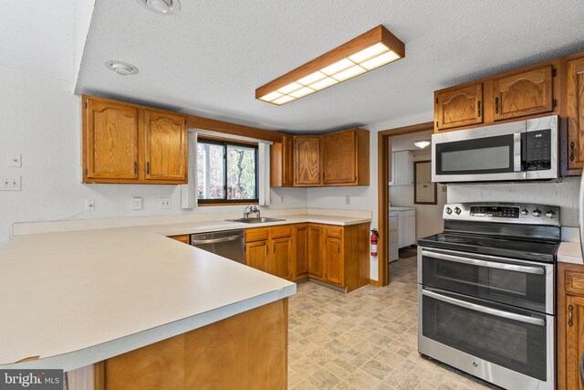 kitchen with kitchen peninsula, appliances with stainless steel finishes, a textured ceiling, and washer and clothes dryer