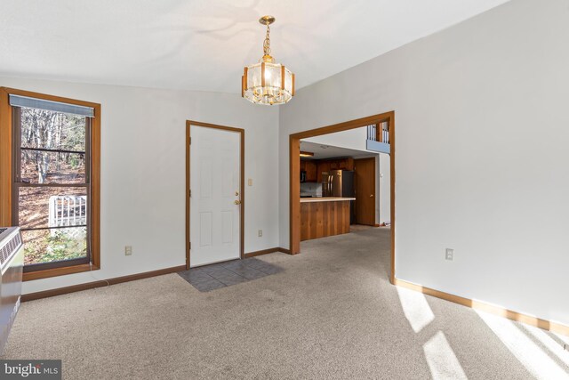 spare room featuring light carpet, a healthy amount of sunlight, vaulted ceiling, and a notable chandelier