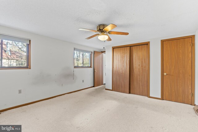 unfurnished bedroom featuring carpet, a textured ceiling, ceiling fan, and multiple closets