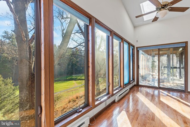 unfurnished sunroom with ceiling fan, vaulted ceiling with skylight, and a baseboard radiator