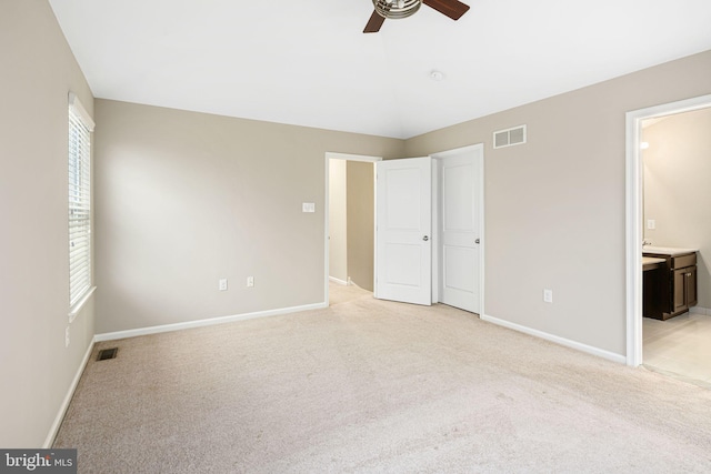 unfurnished bedroom featuring light colored carpet, ensuite bath, and ceiling fan