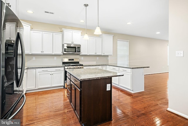 kitchen featuring appliances with stainless steel finishes, light stone counters, pendant lighting, hardwood / wood-style flooring, and a kitchen island