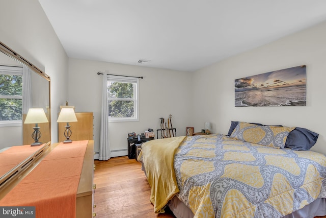 bedroom with light hardwood / wood-style flooring and a baseboard heating unit