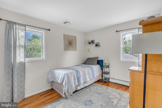 bedroom featuring multiple windows, hardwood / wood-style flooring, and baseboard heating