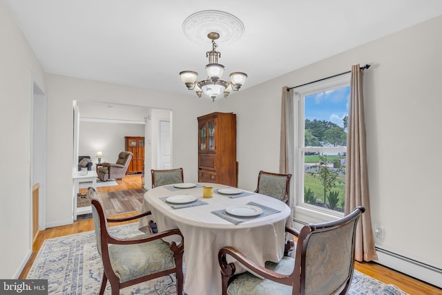 dining space with light hardwood / wood-style flooring, a baseboard heating unit, and a notable chandelier