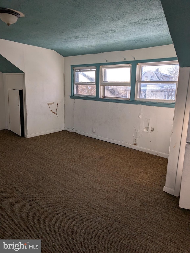 spare room with a textured ceiling and dark colored carpet