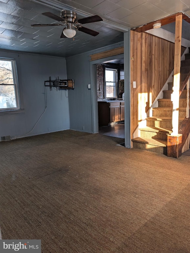 unfurnished living room featuring carpet, a wealth of natural light, visible vents, and stairway
