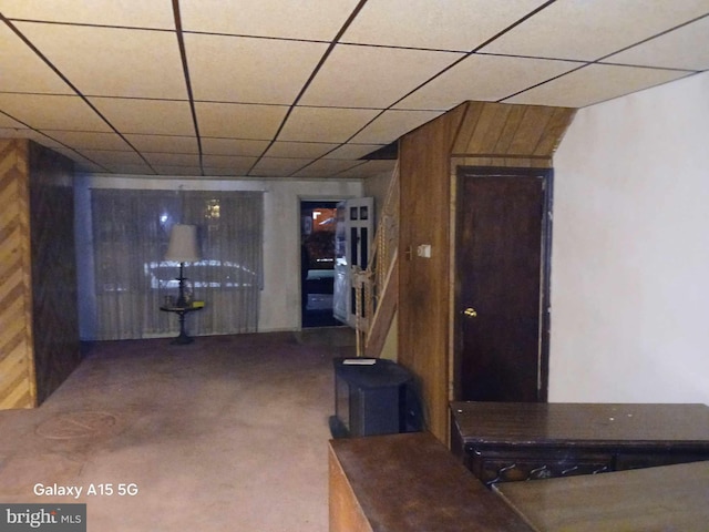 basement with carpet flooring, a paneled ceiling, and wooden walls