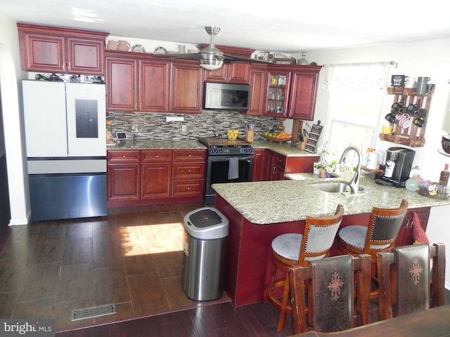 kitchen with sink, dark wood-type flooring, stainless steel appliances, light stone counters, and kitchen peninsula