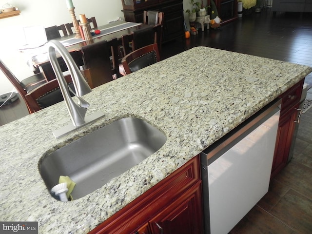 kitchen featuring dishwashing machine, dark hardwood / wood-style floors, light stone counters, and sink