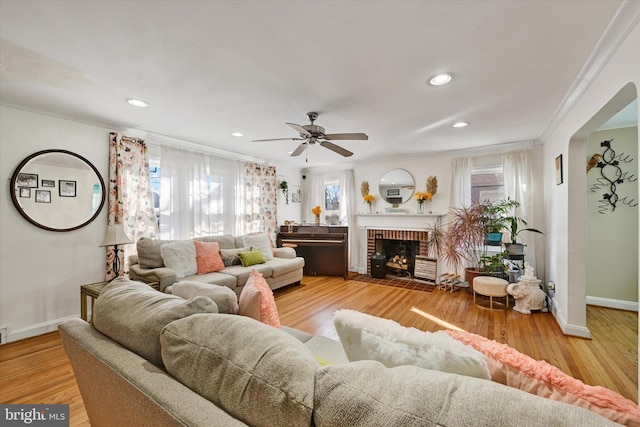 living room with ceiling fan, ornamental molding, a fireplace, and light hardwood / wood-style flooring