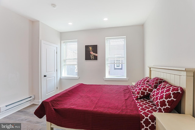 bedroom featuring hardwood / wood-style flooring, baseboard heating, and multiple windows