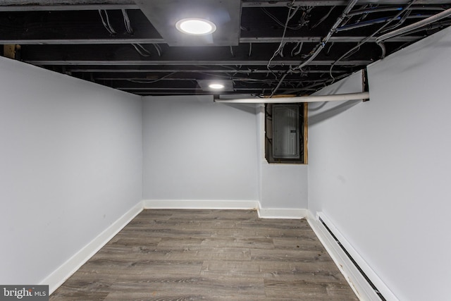 basement featuring electric panel, baseboard heating, and dark hardwood / wood-style flooring