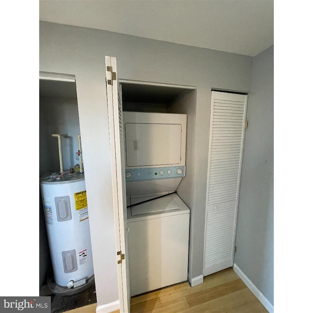 laundry room featuring water heater, stacked washer / dryer, and wood-type flooring