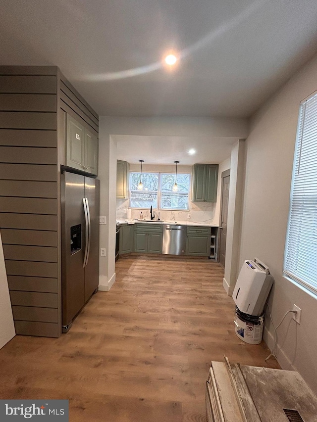 kitchen with light wood-type flooring, pendant lighting, sink, and stainless steel appliances