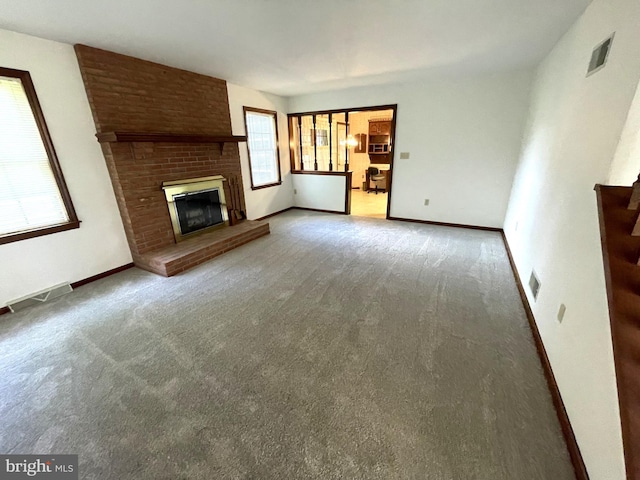 unfurnished living room with a brick fireplace, carpet flooring, and plenty of natural light