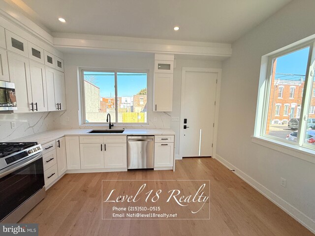 kitchen with tasteful backsplash, appliances with stainless steel finishes, white cabinetry, a sink, and light wood-style floors