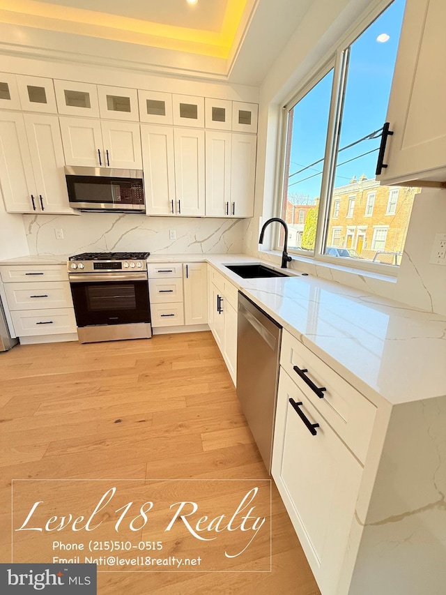 kitchen featuring white cabinetry, a sink, appliances with stainless steel finishes, and light stone counters