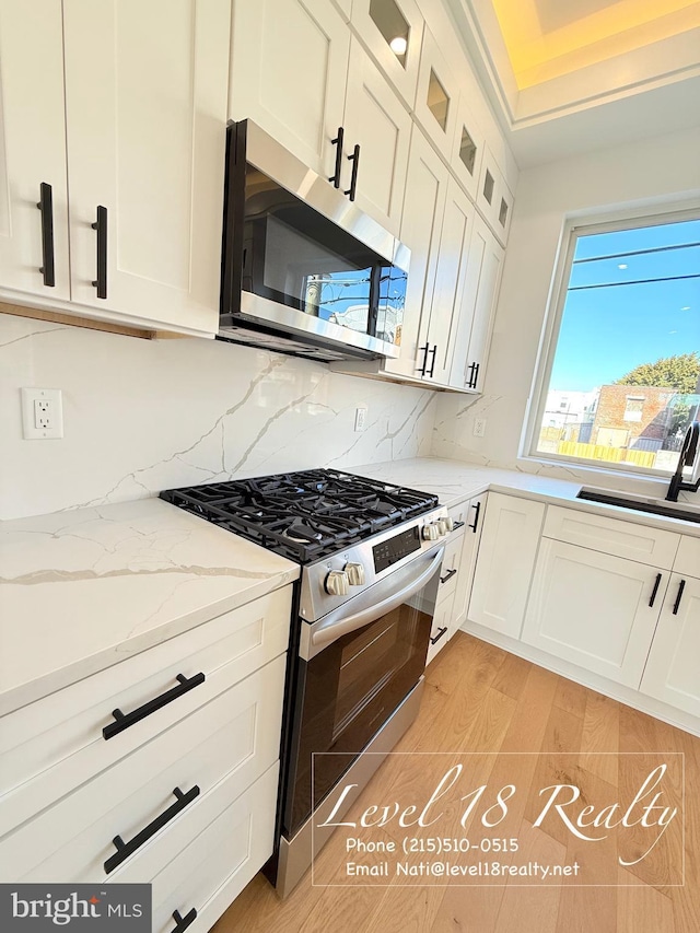 kitchen with decorative backsplash, white cabinets, a sink, and appliances with stainless steel finishes