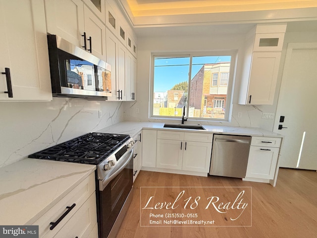kitchen with stainless steel appliances, a sink, light stone counters, white cabinets, and glass insert cabinets