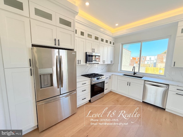 kitchen with a sink, light wood-type flooring, white cabinets, and appliances with stainless steel finishes