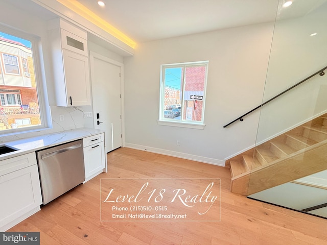 kitchen featuring light wood-style flooring, baseboards, white cabinetry, light stone counters, and stainless steel dishwasher
