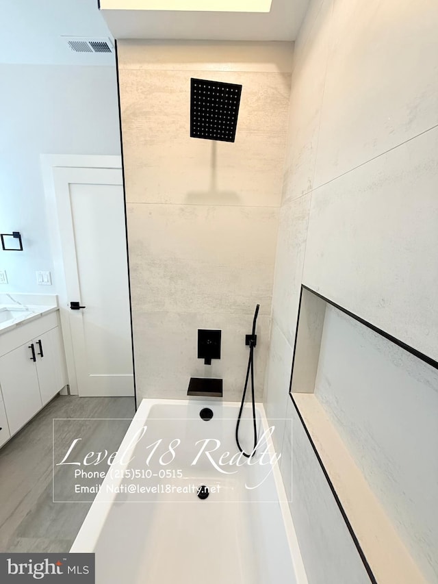 full bathroom with vanity, tiled shower, and visible vents