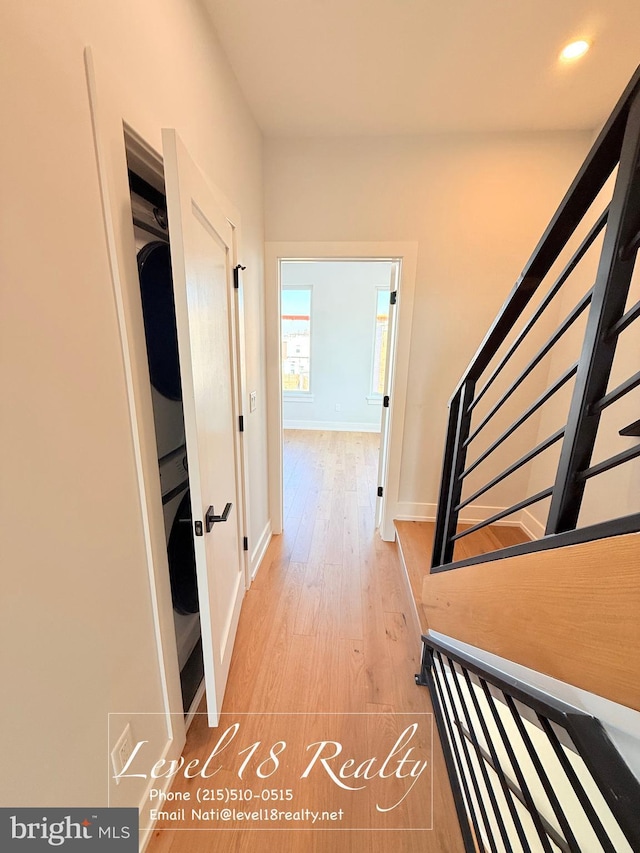 hallway featuring stacked washer and clothes dryer, stairs, baseboards, recessed lighting, and light wood-type flooring