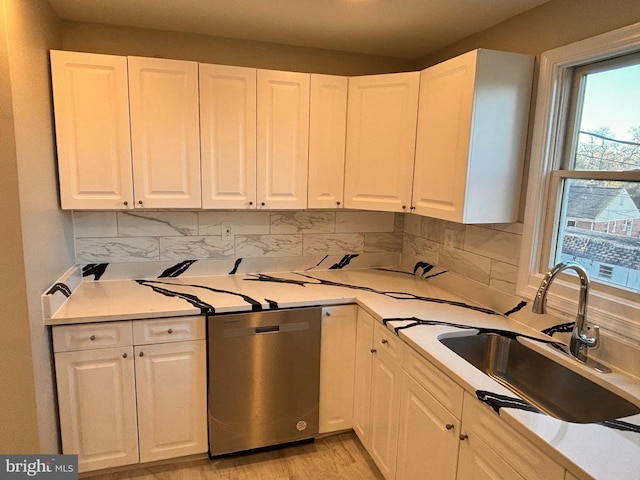 kitchen with stainless steel dishwasher, decorative backsplash, white cabinetry, and sink