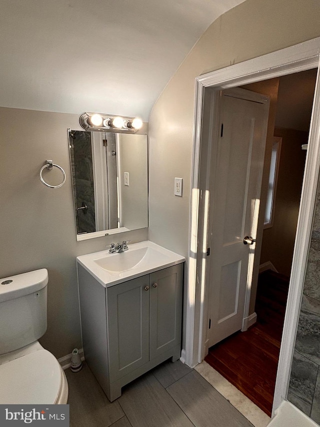 bathroom with hardwood / wood-style floors, vanity, toilet, and vaulted ceiling