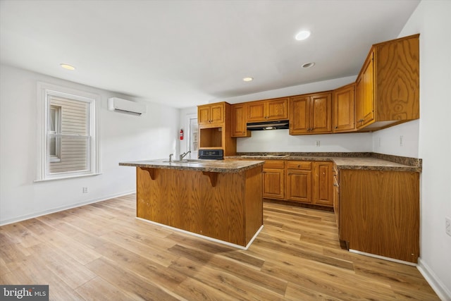 kitchen featuring stovetop, a wall mounted AC, a center island with sink, light wood-type flooring, and a breakfast bar area