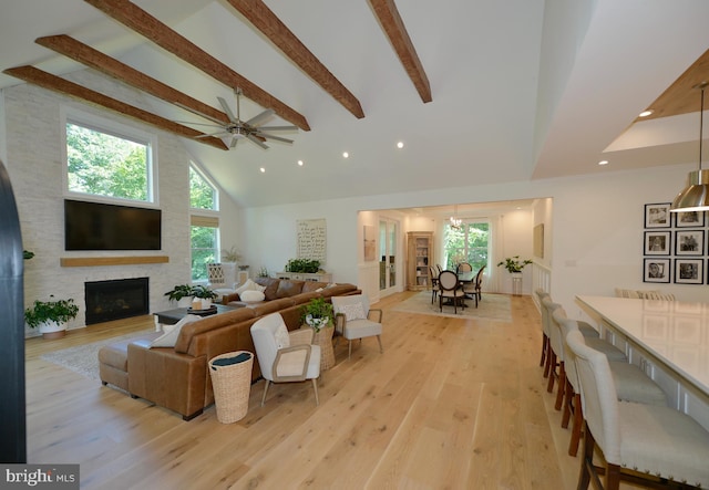 living room featuring beam ceiling, high vaulted ceiling, a large fireplace, light hardwood / wood-style floors, and ceiling fan with notable chandelier