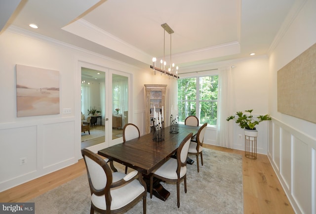 dining space featuring a raised ceiling, a notable chandelier, light hardwood / wood-style floors, and crown molding