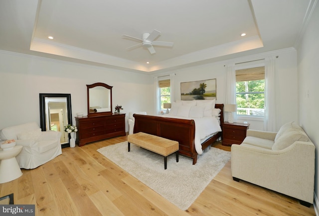 bedroom featuring ceiling fan, multiple windows, light hardwood / wood-style floors, and a raised ceiling