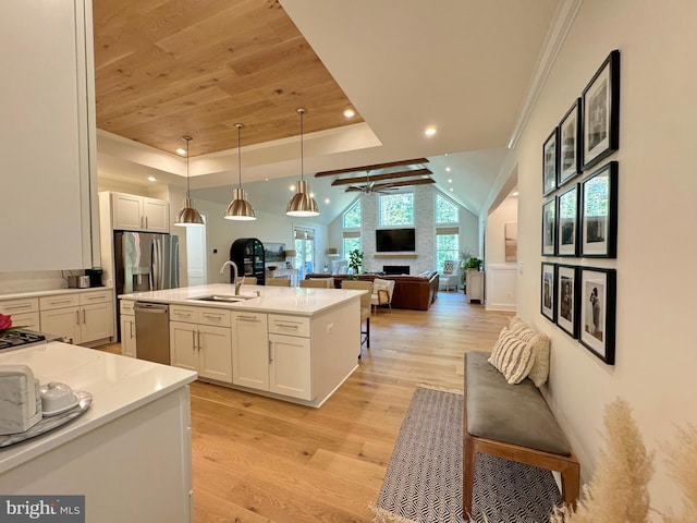 kitchen with a kitchen island with sink, white cabinetry, pendant lighting, sink, and light hardwood / wood-style flooring