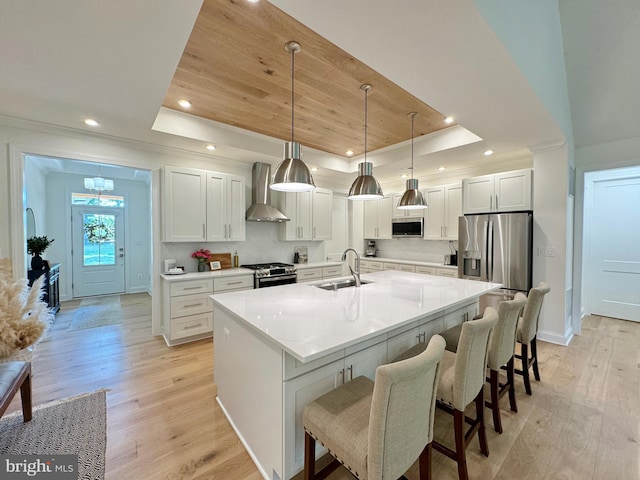 kitchen featuring light hardwood / wood-style flooring, wall chimney range hood, sink, and a raised ceiling