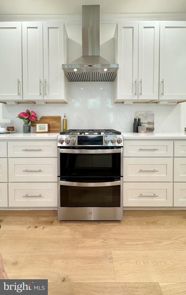 kitchen featuring white cabinets, wall chimney exhaust hood, and stainless steel gas range