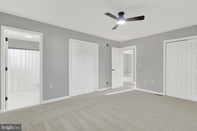 unfurnished bedroom with ensuite bathroom, ceiling fan, light carpet, and two closets