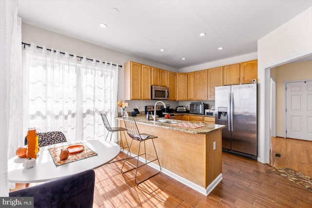 kitchen featuring light stone countertops, sink, kitchen peninsula, light hardwood / wood-style floors, and stainless steel appliances