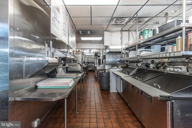 kitchen with dark tile patterned floors, stainless steel counters, and a paneled ceiling