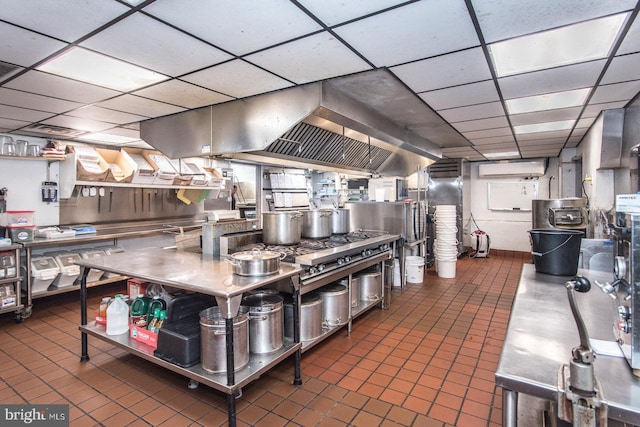 kitchen with a paneled ceiling, an AC wall unit, stainless steel counters, and dark tile patterned flooring